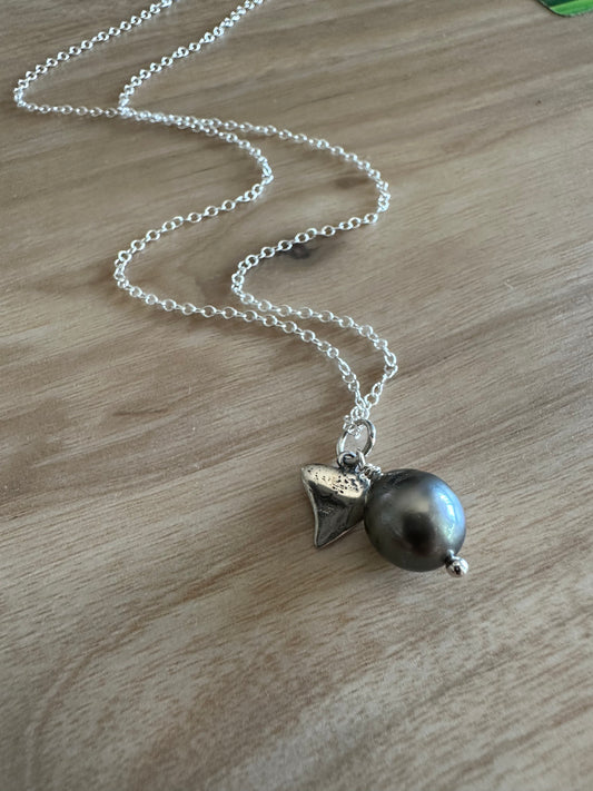 black peral and silver sharks tooth pendant on a silver shain lays on a wooden background
