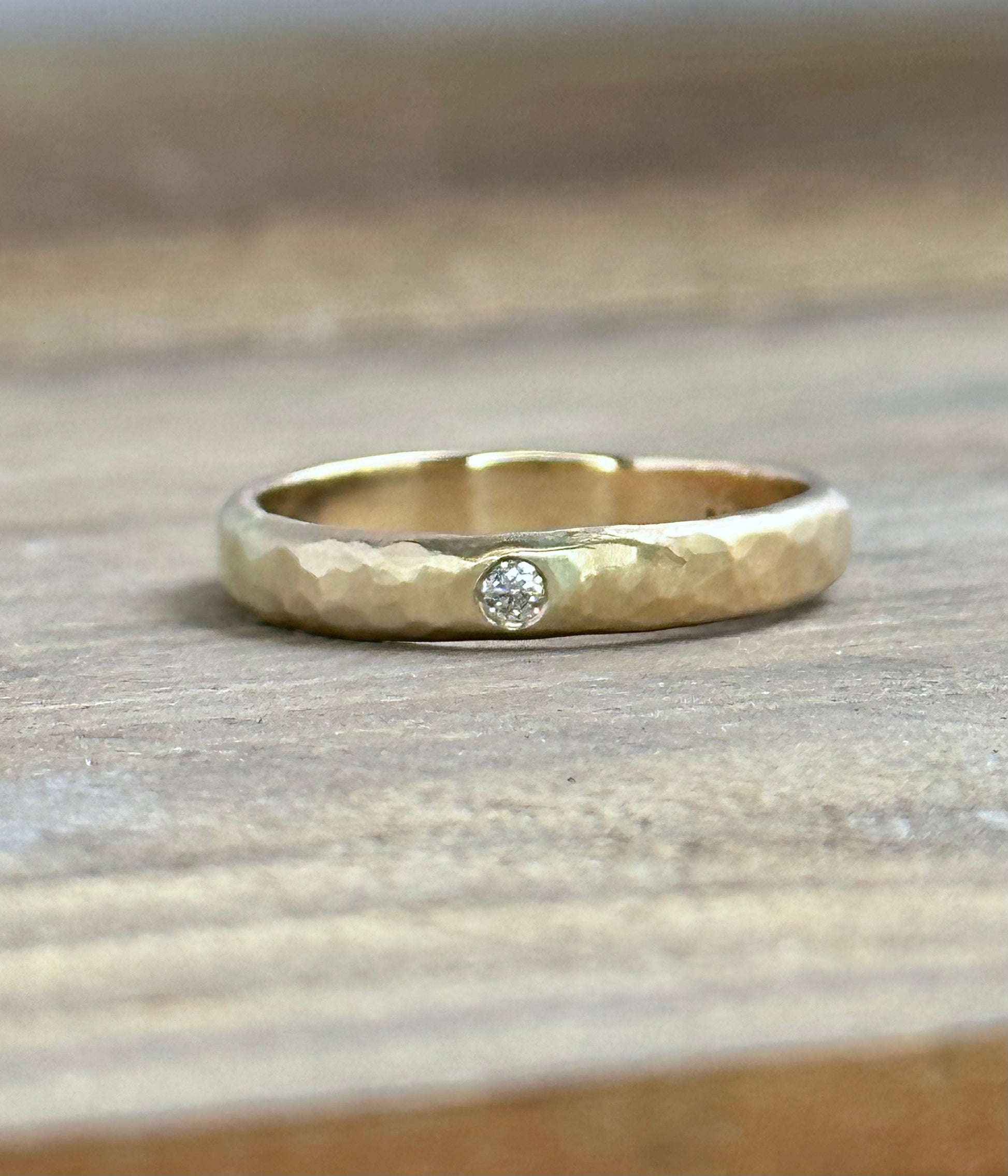 a gold textured ring iwth a single white diamond sits on a wooden background