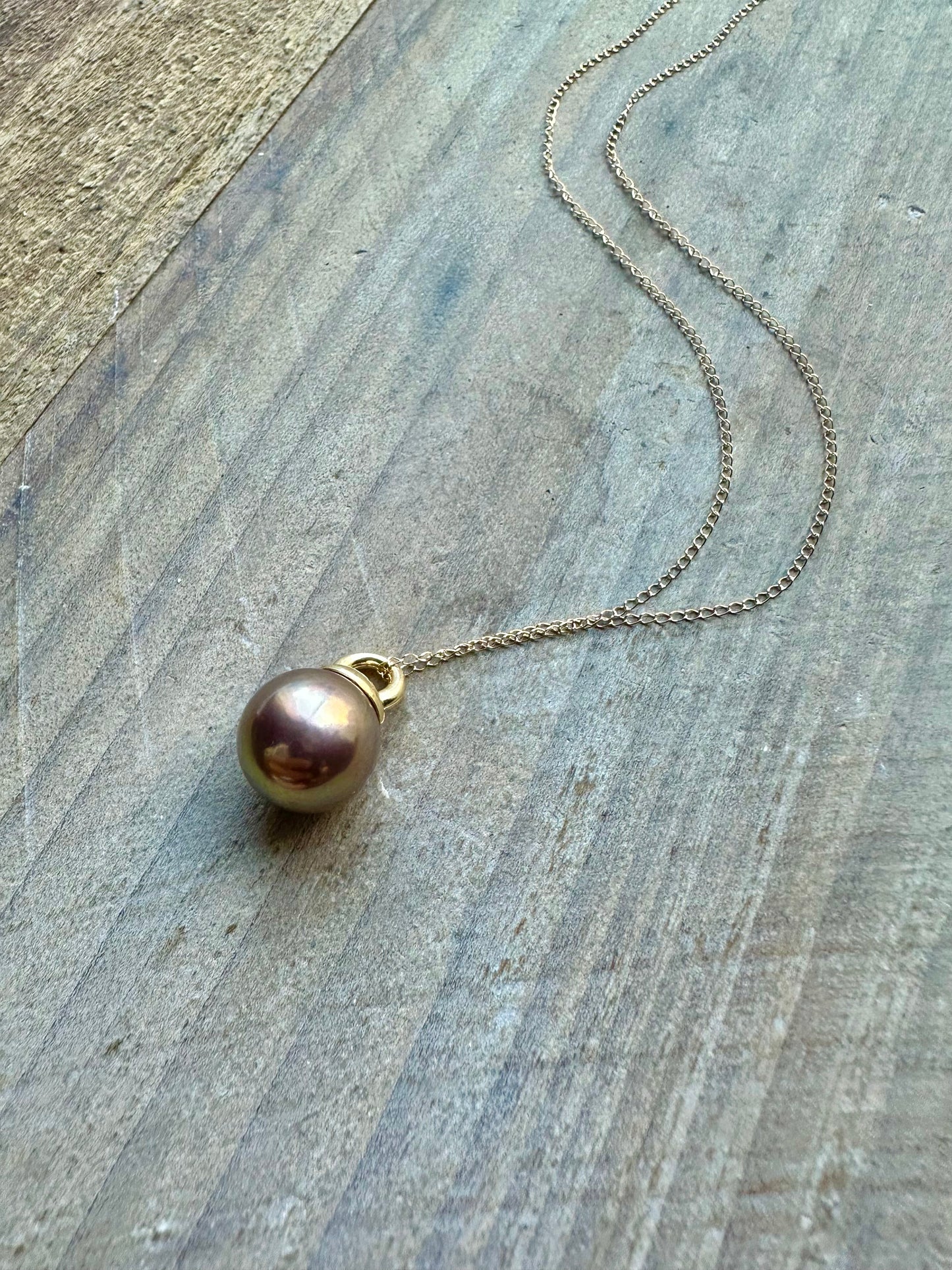 a copery pink round pearl necklace on a gold chain is on a grey wooden background