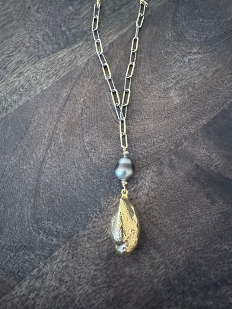 the back of a geode and black pearl on a gold and silver chain on a grey wooden background