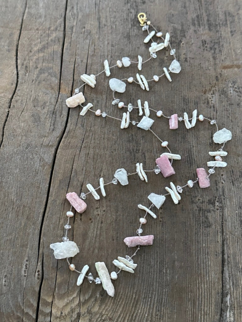 a silk knotted necklace with pink chunky raw tourmaline and white perals with herkimer diamonds sits on a wooden background