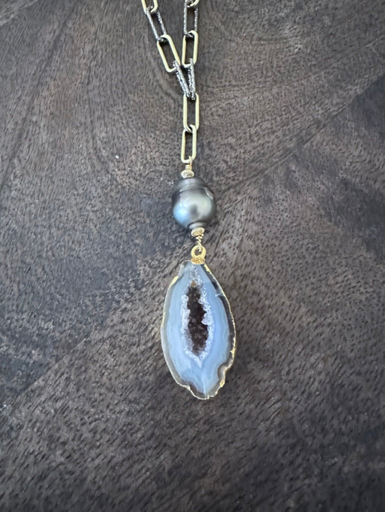 a close up of geode and black pearl on a gold and silver chain on a grey wooden background