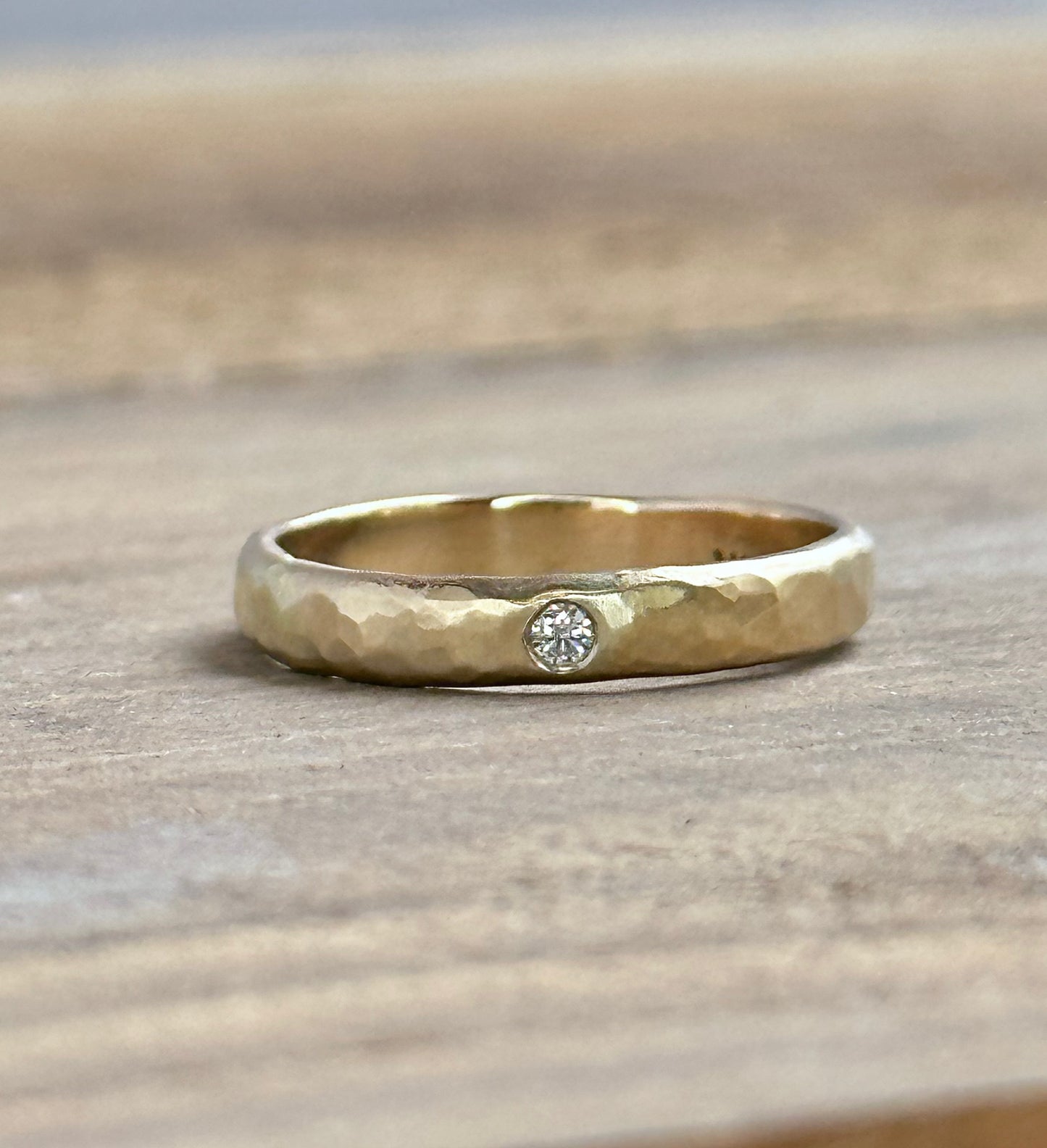 a gold textured ring iwth a single white diamond sits on a wooden background