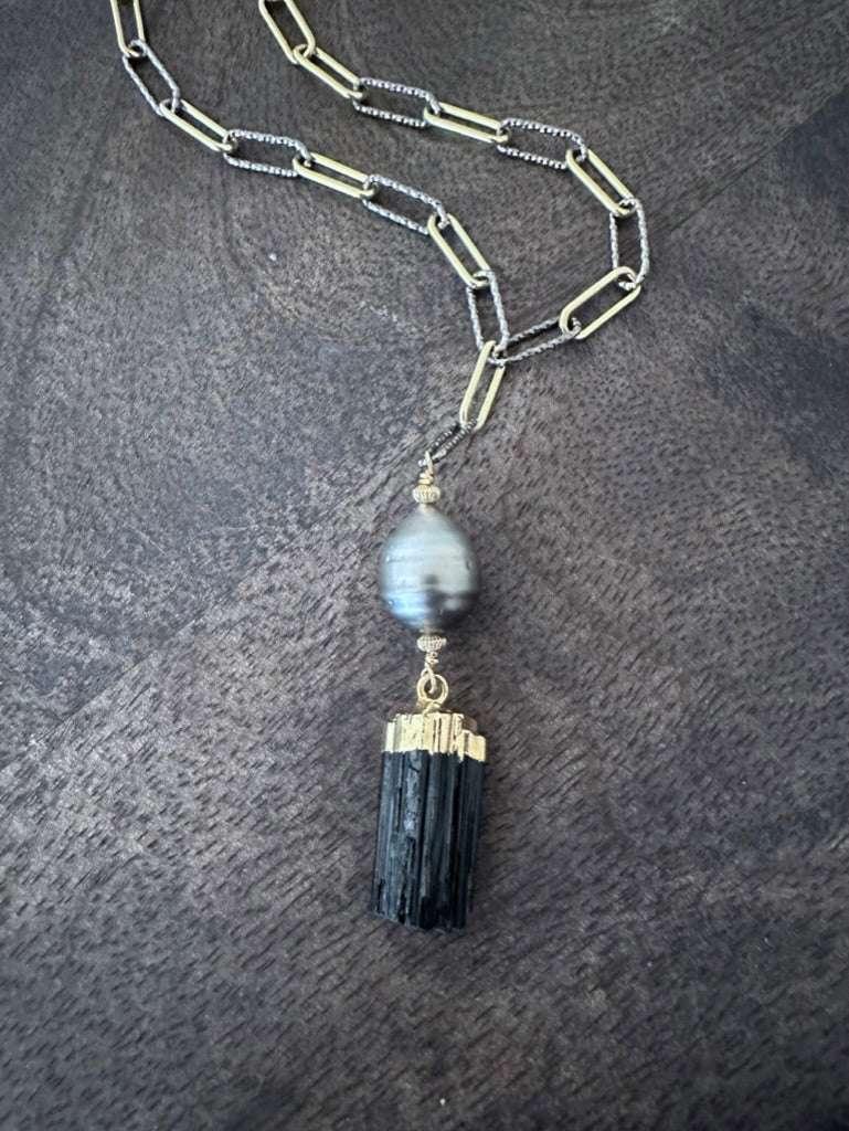 a black raw tourmaline and tahitian pearl pendand on a mixed gold and silver paperclip chain on a wooden background