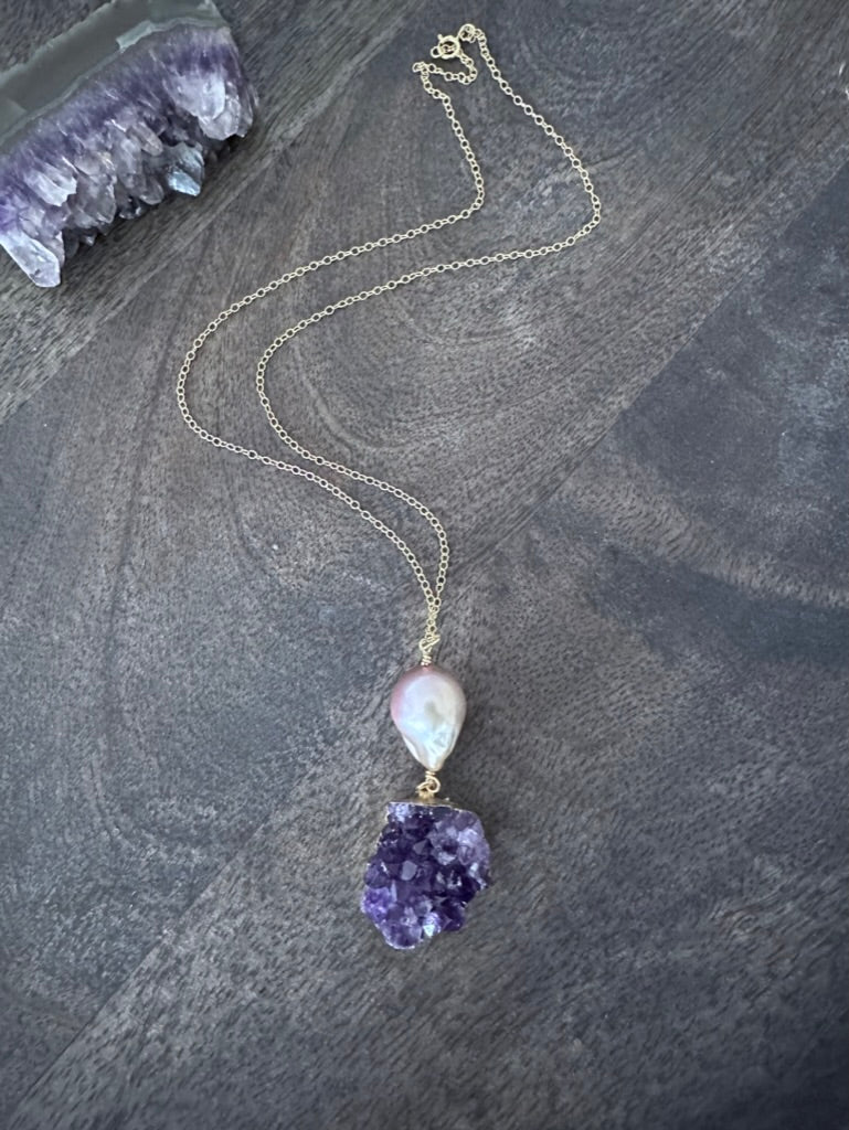 a large pink fireball shaped pearl with a purple amethyst cluster on a gold chan lays on a wooden background
