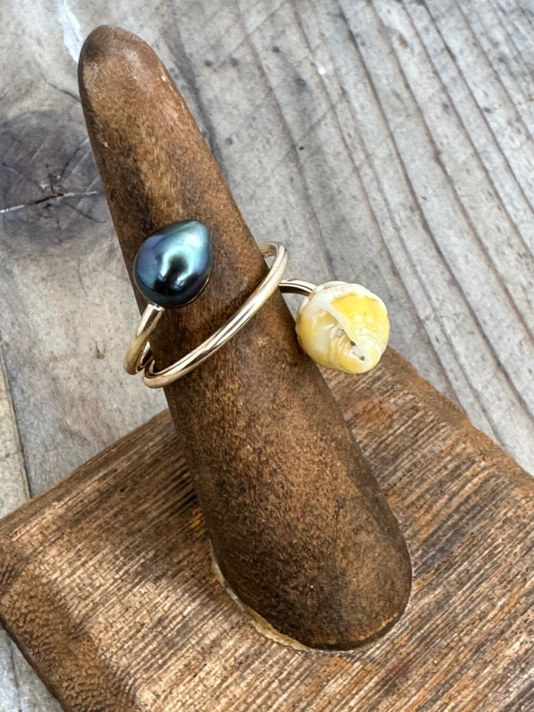 a ring on a wooden ring stand with a yellow shell and a black peral on a gold wire that twists around the ring holder.