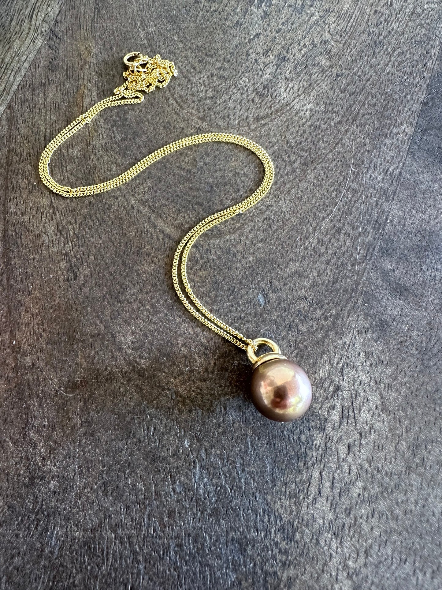 a copery pink round pearl necklace on a gold chain is on a grey wooden background