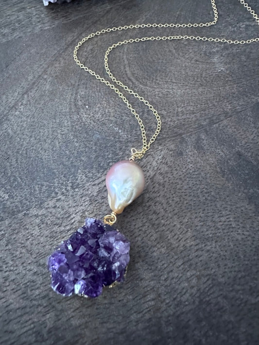 a large pink fireball shaped pearl with a purple amethyst cluster on a gold chan lays on a wooden background