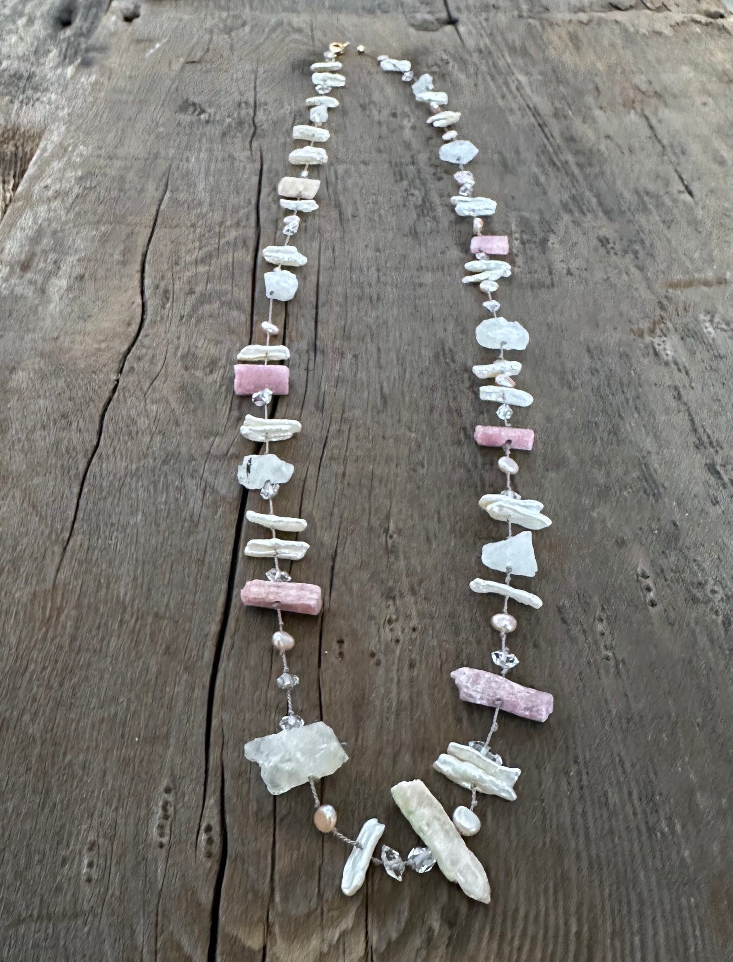 a silk knotted necklace with pink chunky raw tourmaline and white perals with herkimer diamonds sits on a wooden background