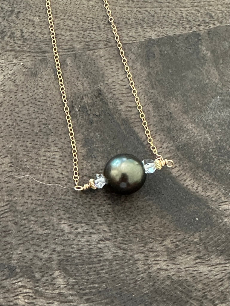 a single black pear with double terminated white crystals on a gold chain on a wooden backgroun d