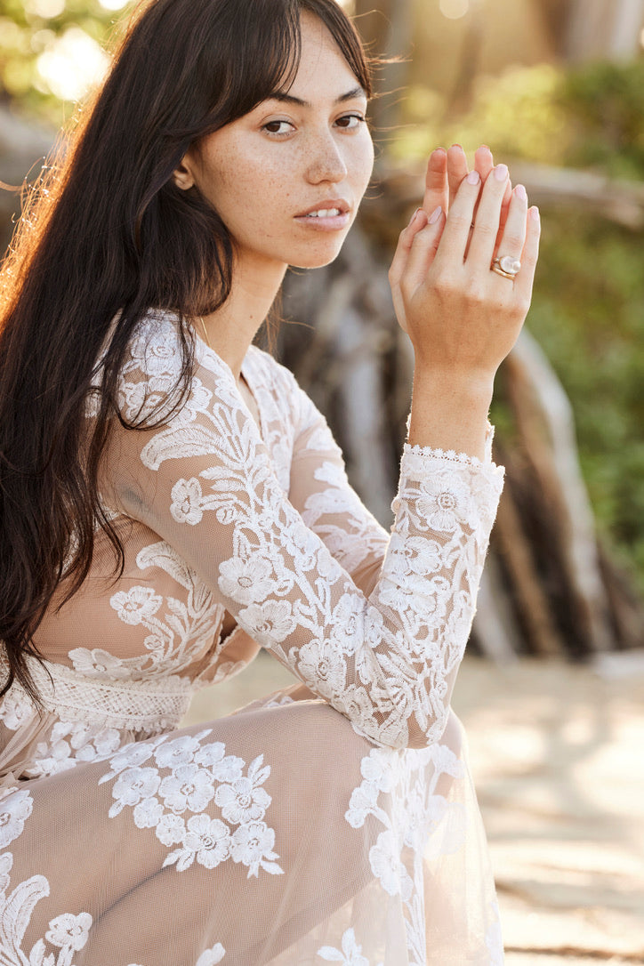a beautiful brown haired woman with a lacydress on has her hand in front of her and is resting them on her knees as she sits. she is wearing a purple ring.