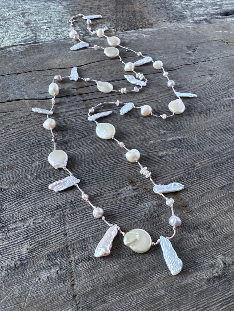 a pinkish silk necklace on a wooden background with odd shaped pearls and round pinky golden pearls