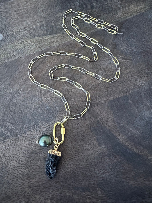 a long necklace wth mixed metal chain with a gold carabeaner and a large black pearl and a raw black tourmaline pendant on a wooden background