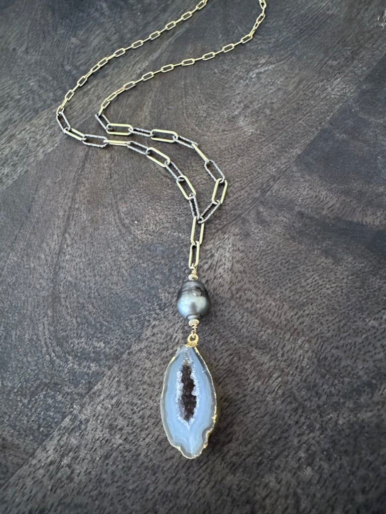 geode and black pearl on a gold and silver chain on a grey wooden background