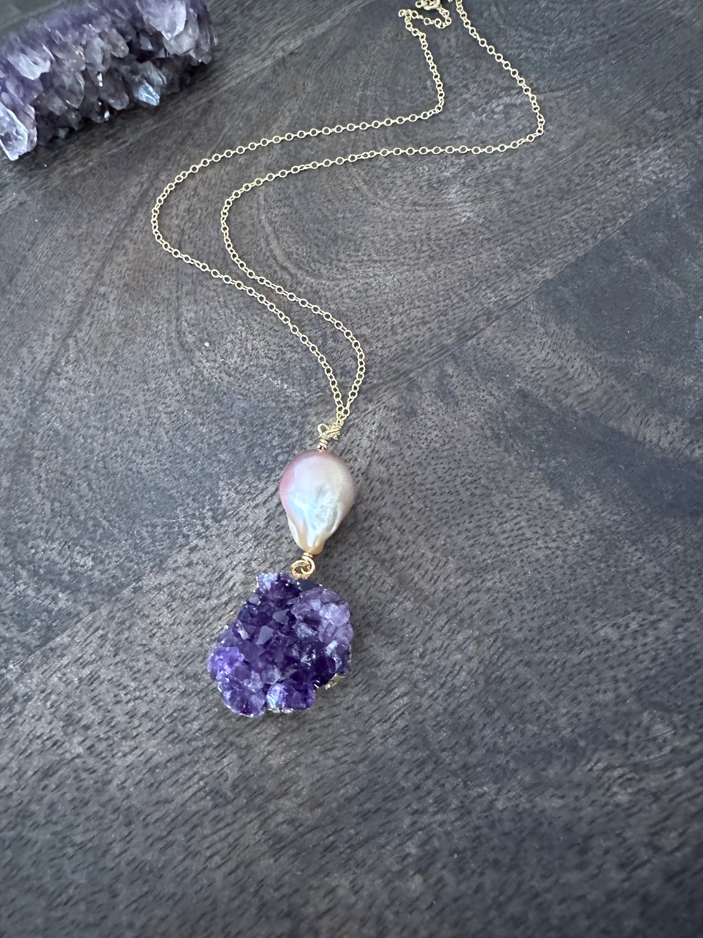 a large pink fireball shaped pearl with a purple amethyst cluster on a gold chan lays on a wooden background