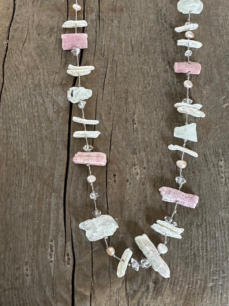 a close up of a silk knotted necklace with pink chunky raw tourmaline and white perals with herkimer diamonds sits on a wooden background