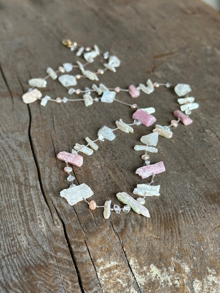 a silk knotted necklace with pink chunky raw tourmaline and white perals with herkimer diamonds sits on a wooden background