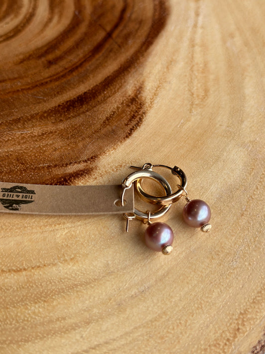 a pair of pink pearls on golden hoops on a warm wooden board.