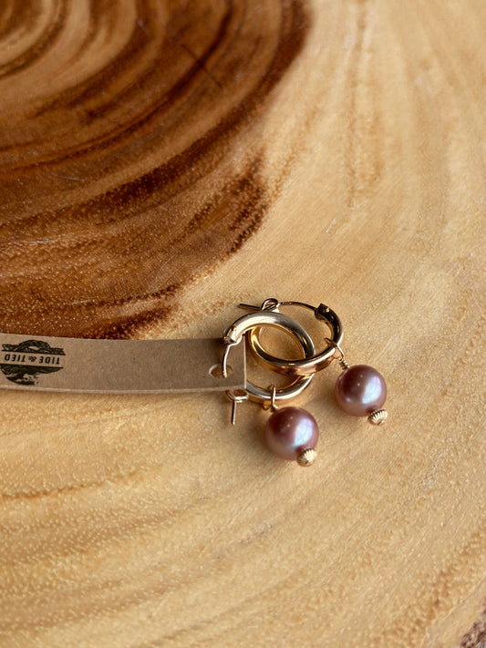 a pair of pink pearls on golden hoops on a warm wooden board. 
