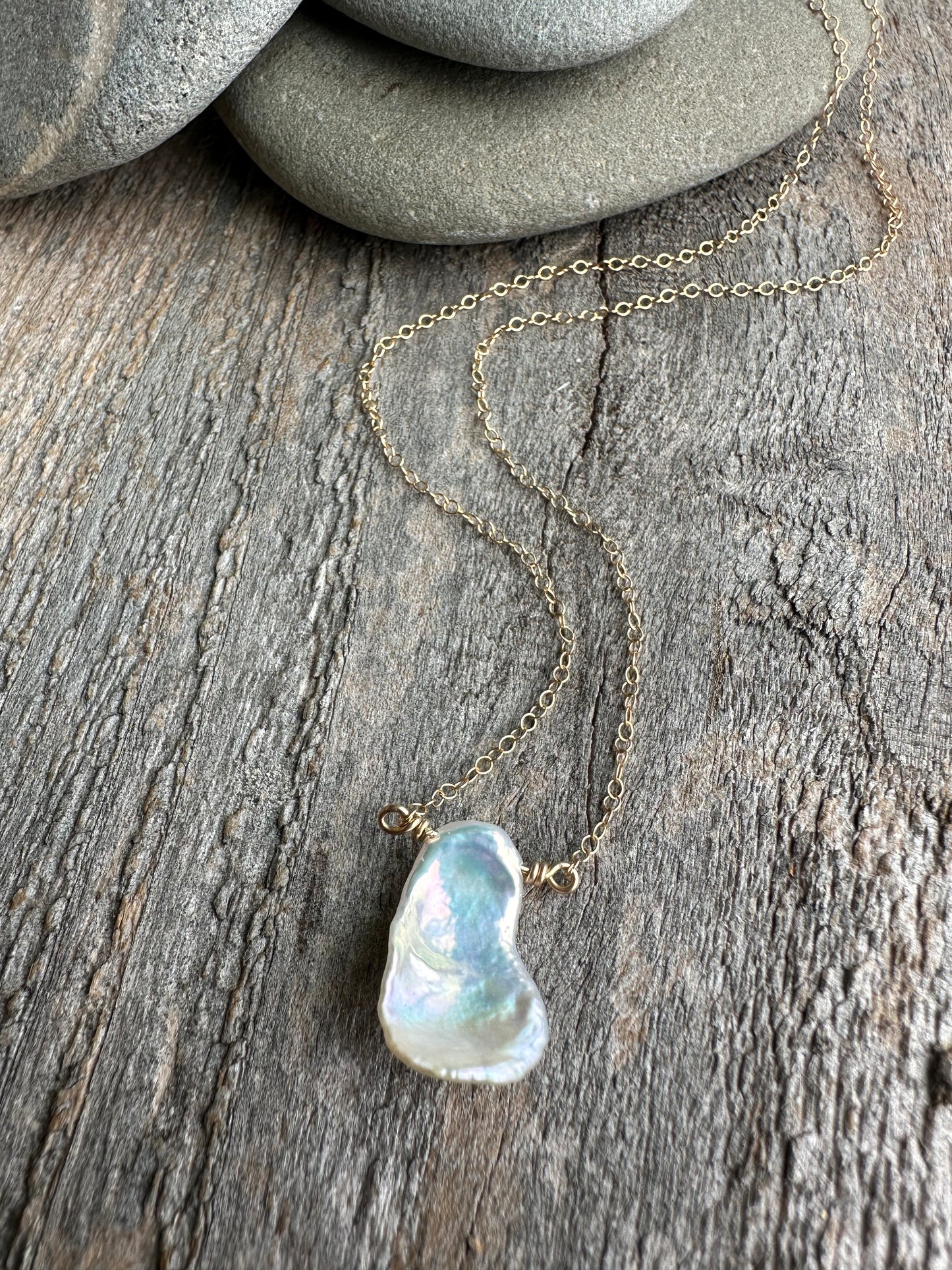 On wooden background there is a gold chain with half inch metallic petal keshi pearl with rocks in upper part of the image.