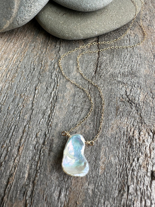 On wooden background there is a gold chain with half inch metallic petal keshi pearl with rocks in upper part of the image.