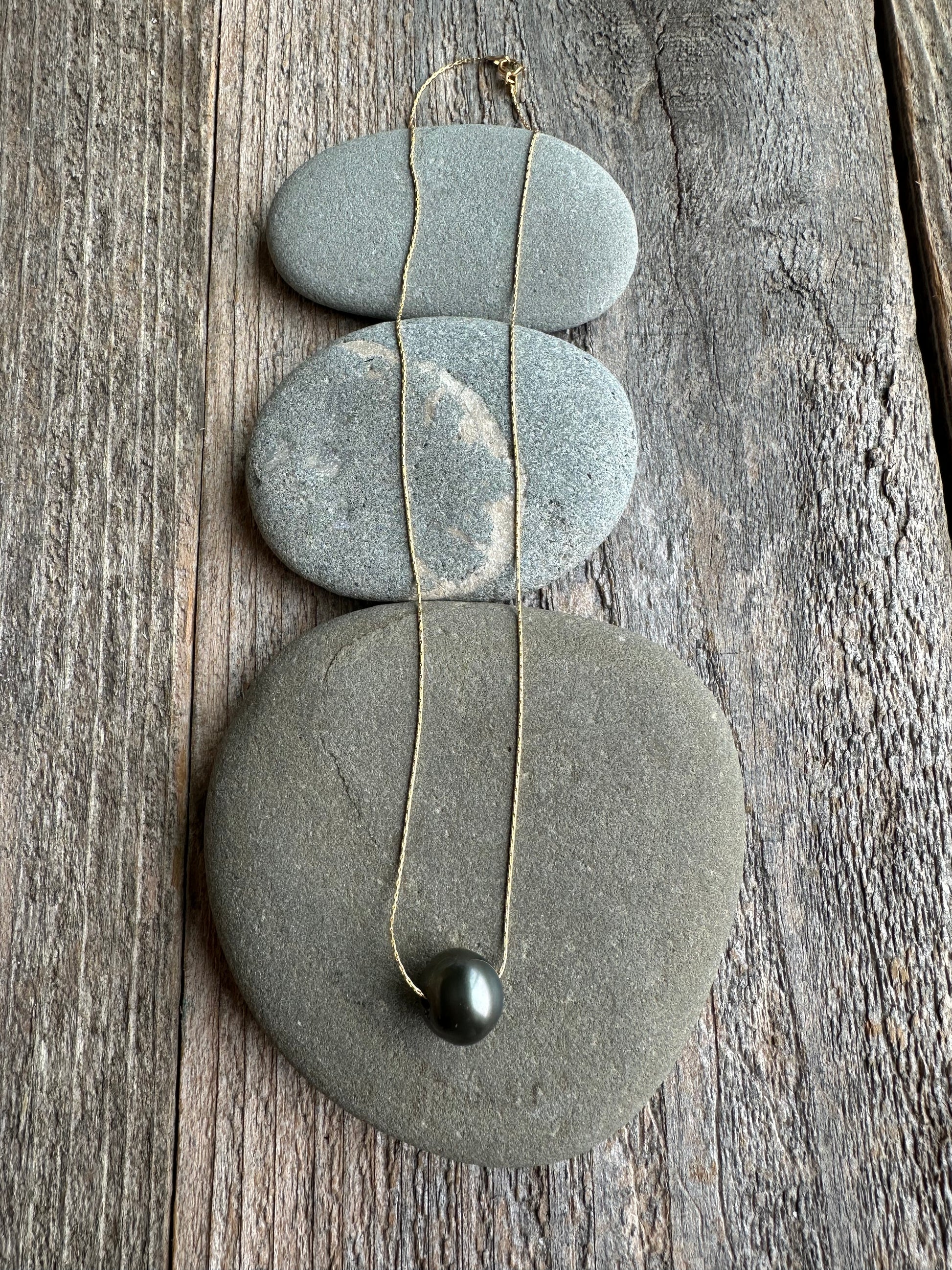 On wooden background theres three rocks with gold chain and Tahitian pearl laid over.