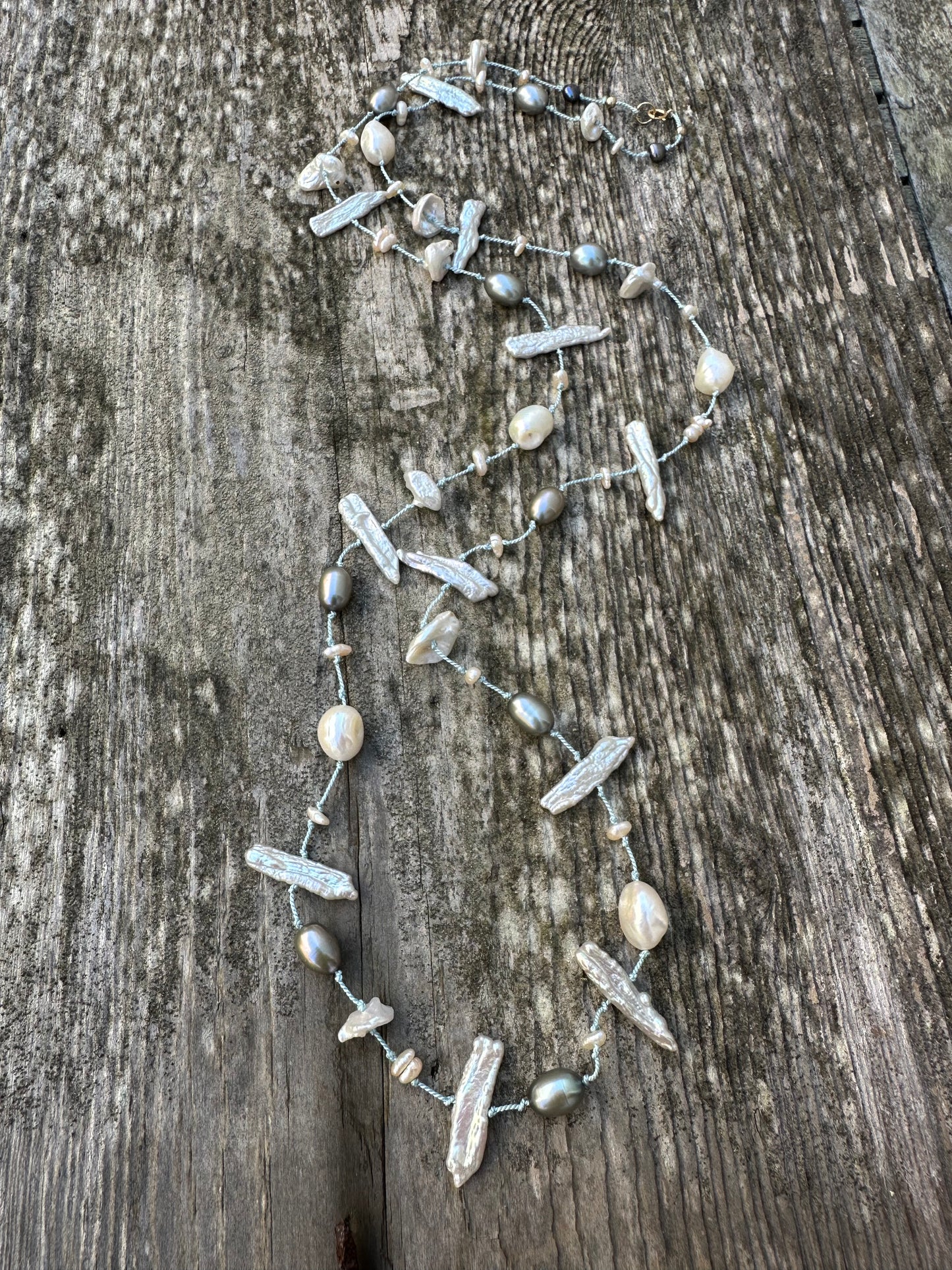 a long silk knotted pearl necklace with white and grey pearls on a wooden backdrop