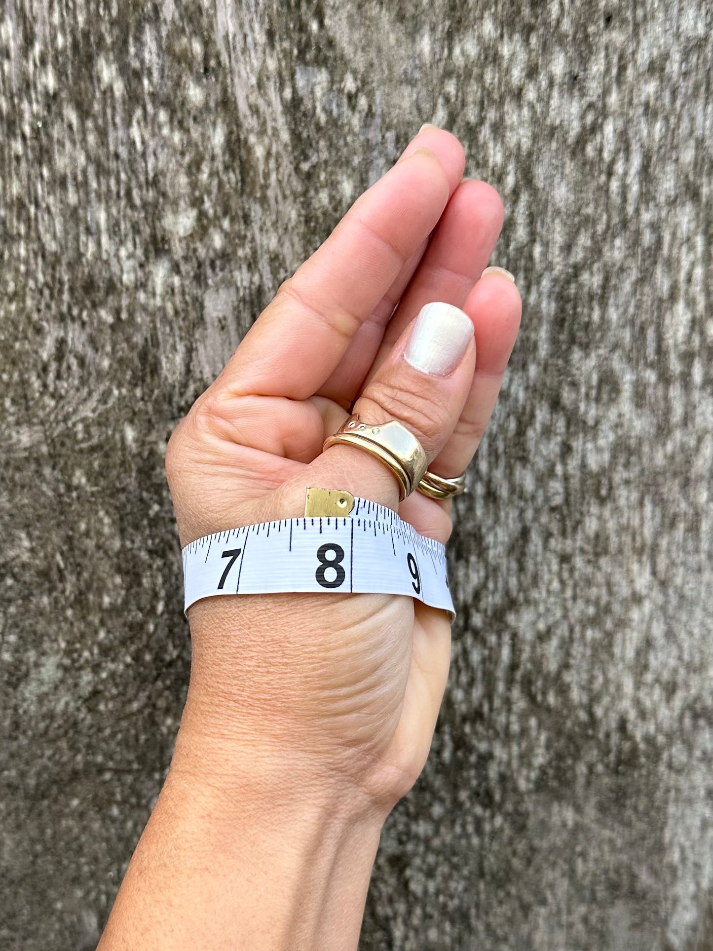 A woman's hand with thumb and pinky touching with a measuring tape wrapped around her palm showing a measurement held up against a wooden back ground.