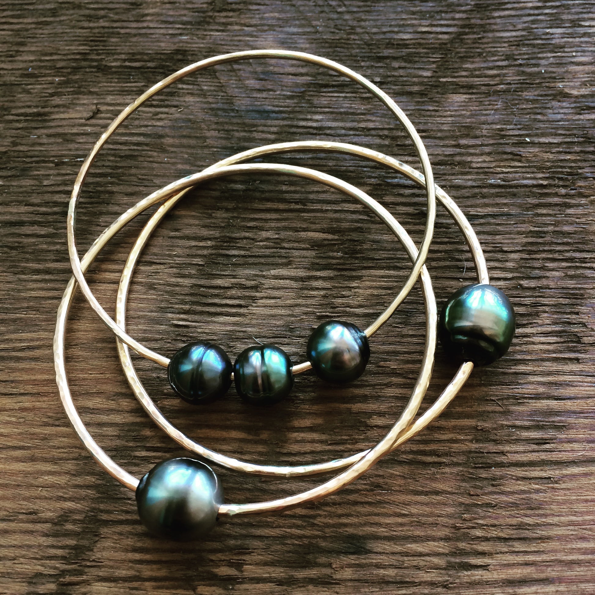 a stack of bangles with black pearls on them lays on a wooden background. two of them have a single bangle and the thied one has three pearls