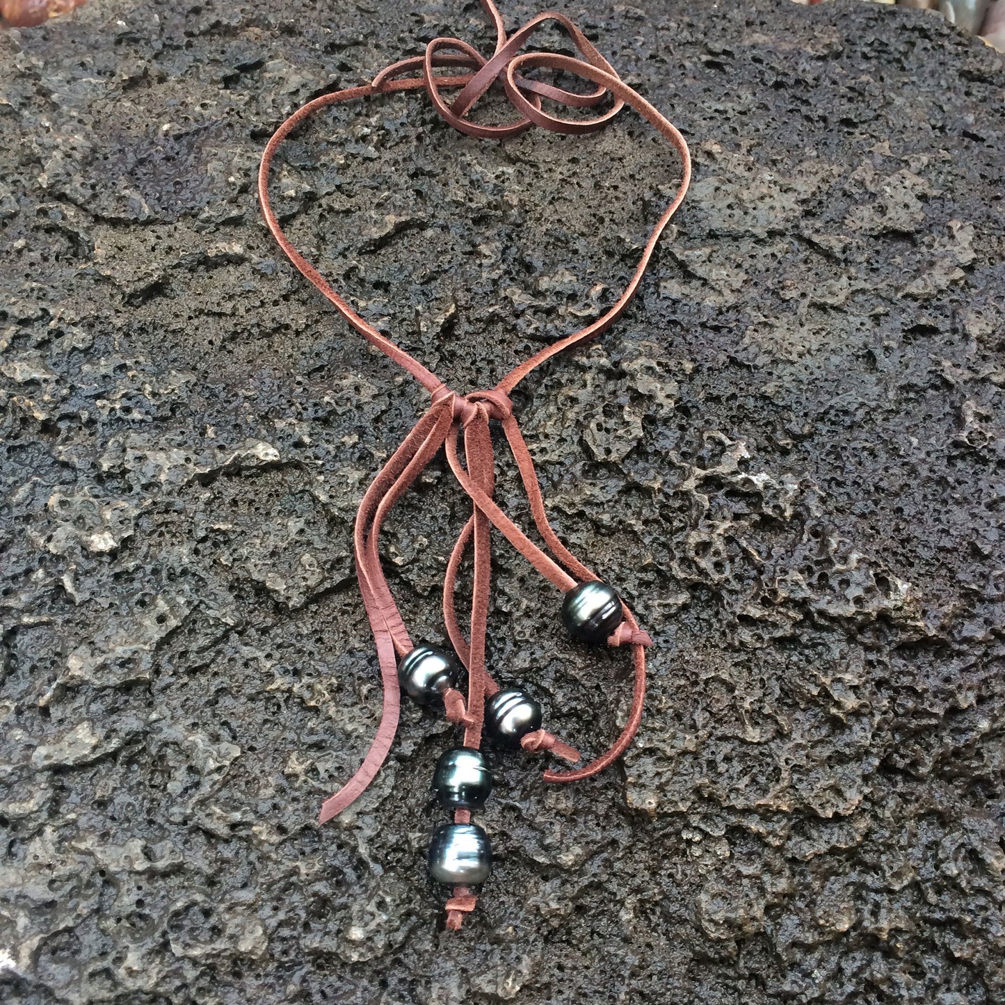 A necklace with strands of brown leather that have Tahtian pros knotted on them on a black stone background