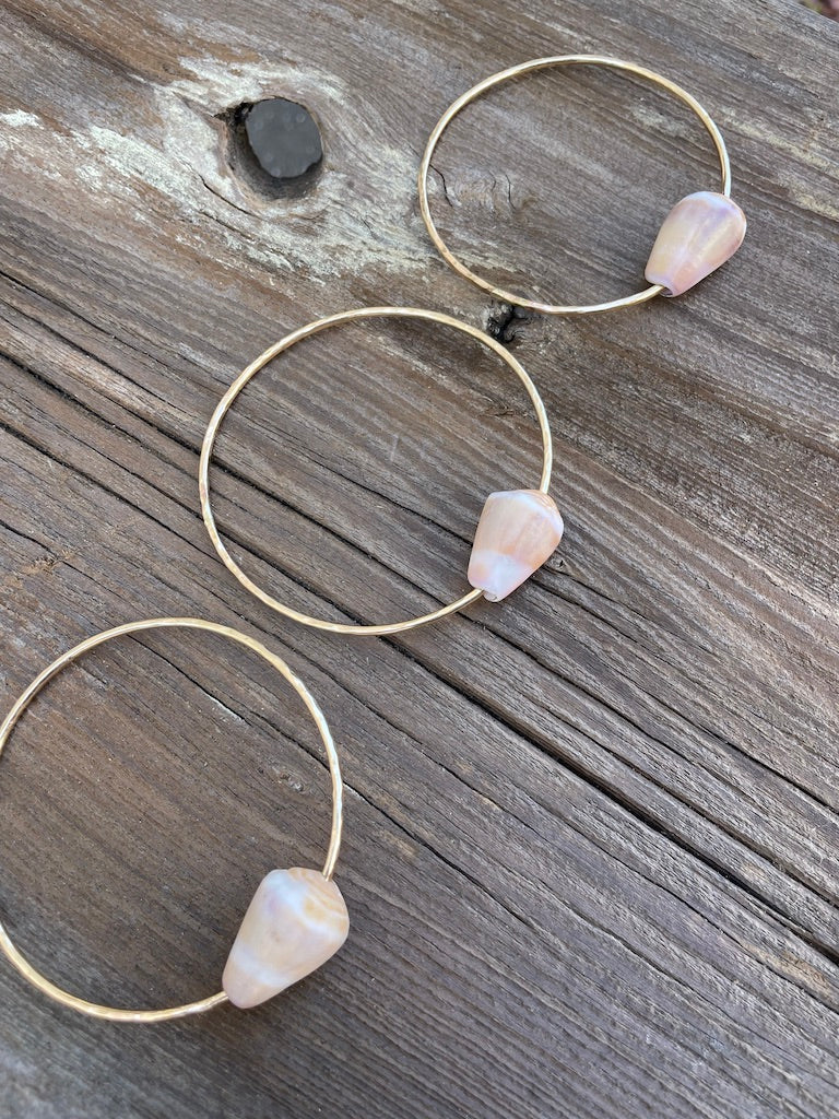 Three gold bangles with cone shells on a wooden background