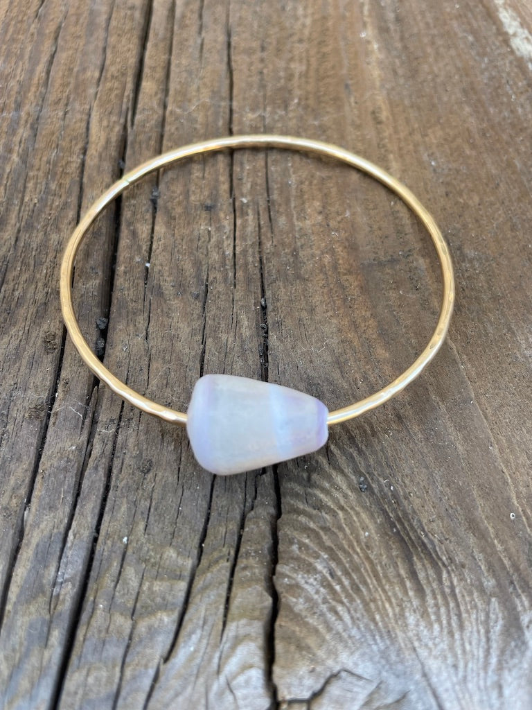 A single gold bangle with a cone shell on a wooden background