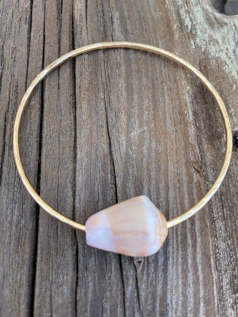 A single gold bangles with a striped cone shell on a wooden background