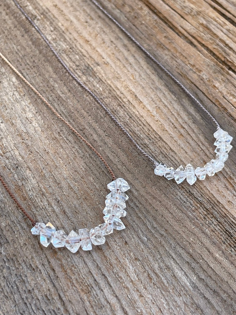 Two herkimer Diamond necklaces one on grey silk and the other on brown silk on a wooden background