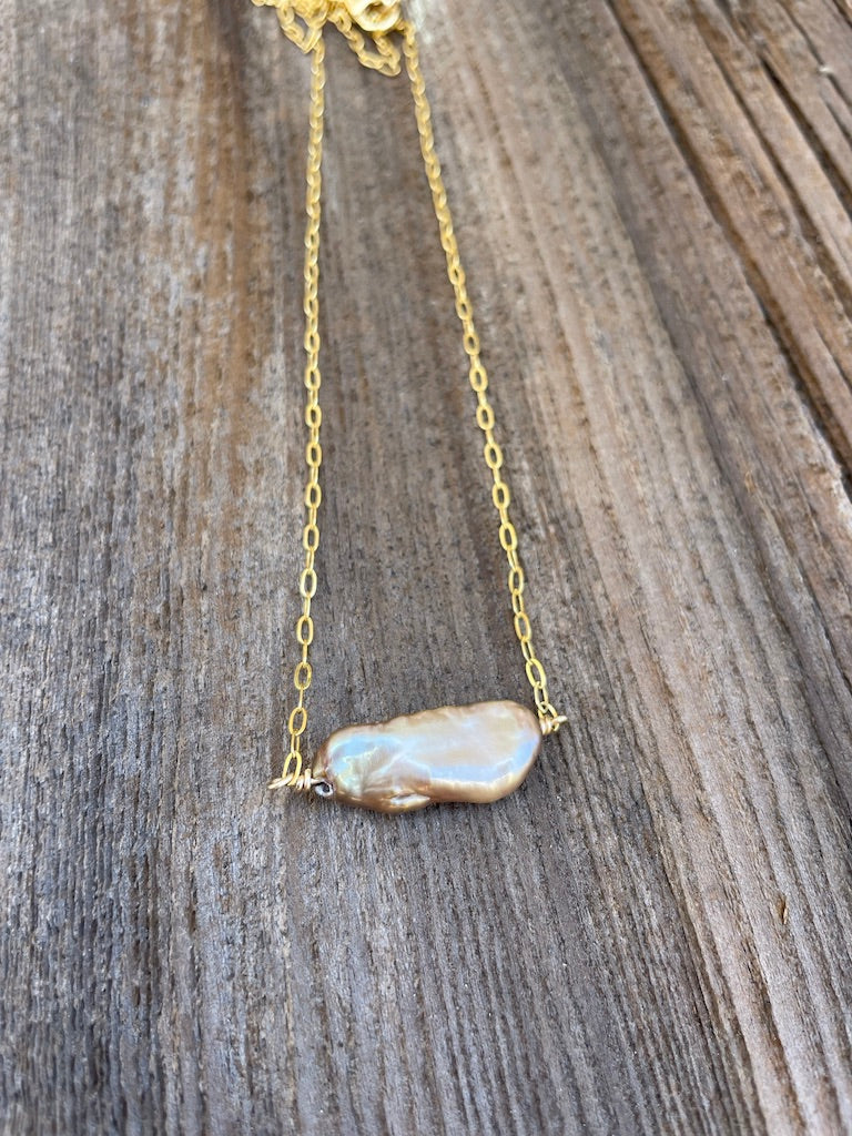 a long silk knotted pearl necklace with white and grey pearls on a wooden backdrop