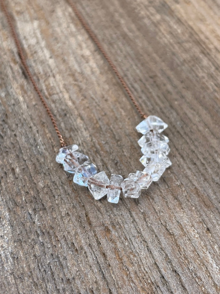 Single row of Herkimer Diamond stones on a brown silk necklace on a wooden background