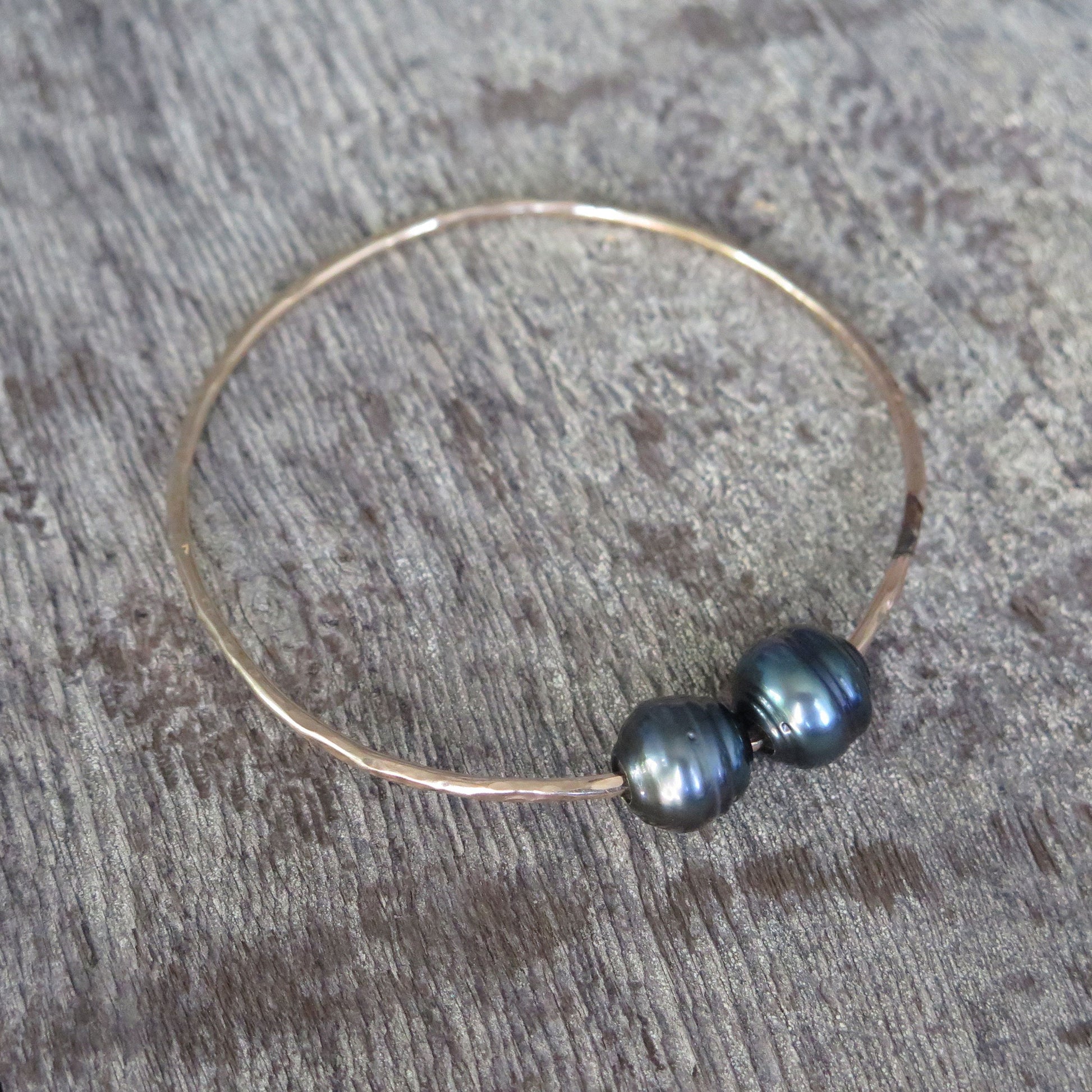 Two black baroque Tahitian pearls on a gold bangle resting on a wooden background