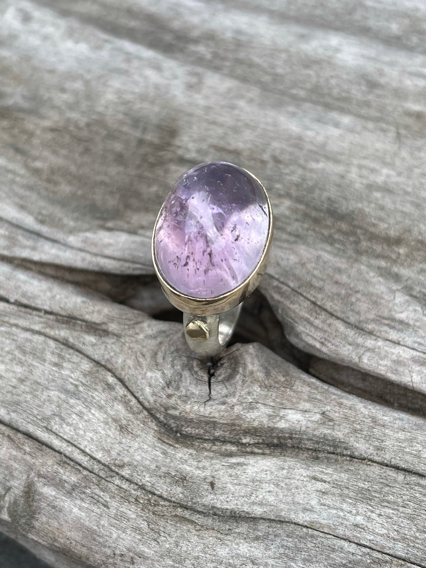 a large purple domes ring with a gold band around it and gold round accent on a silver band sits in some grey wood.