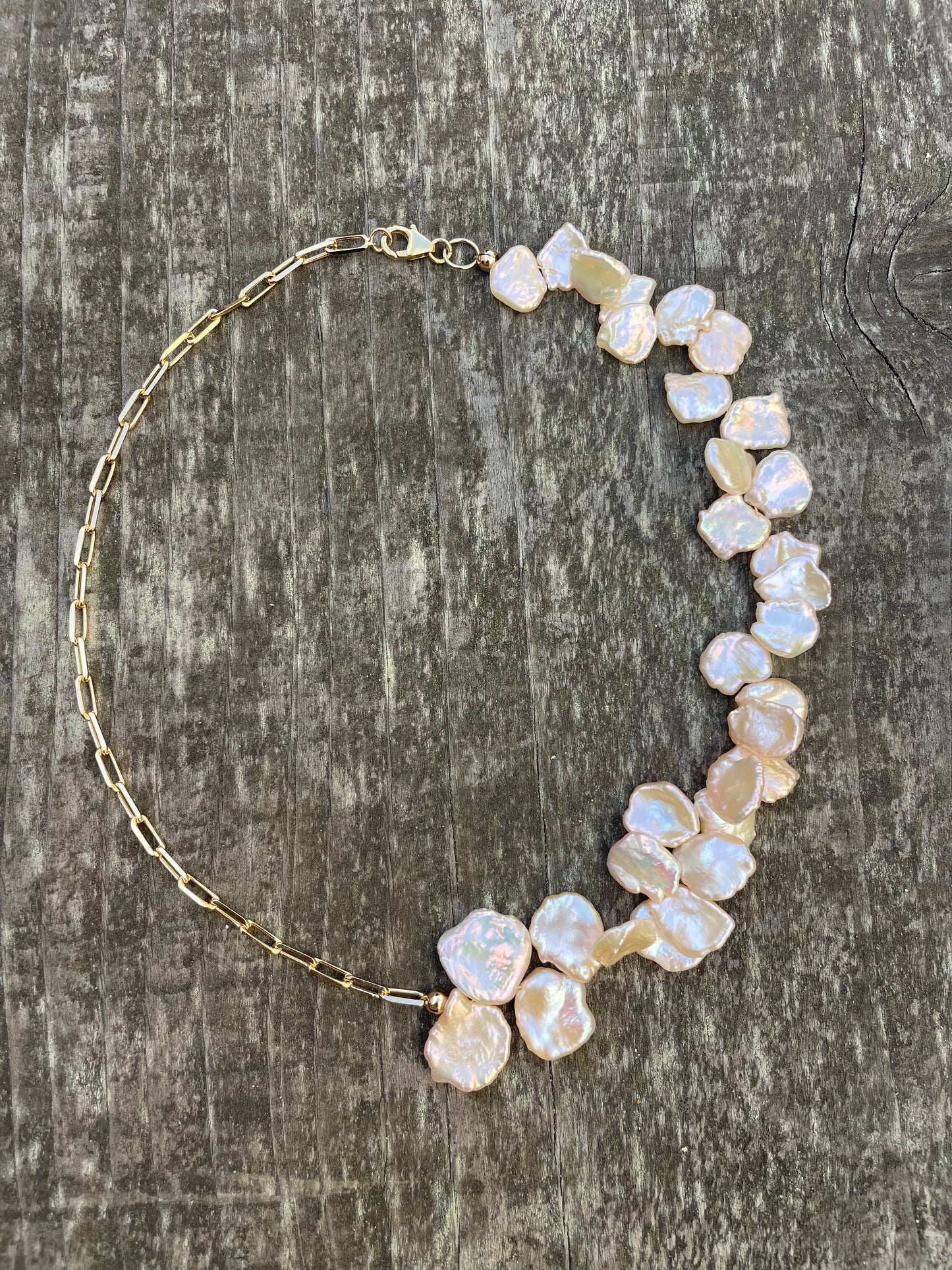 A choker necklace with half gold chain and half pink keshi flat pearls on a wooden background