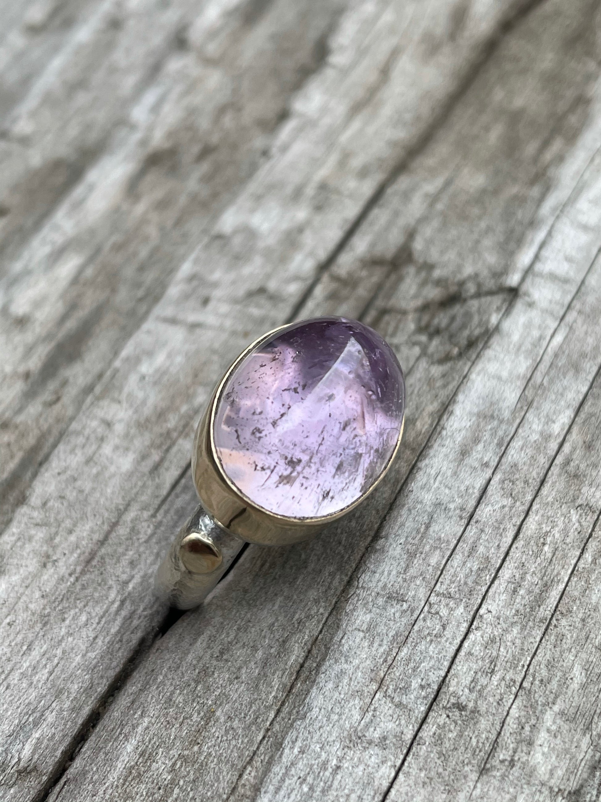 a large purple domes ring with a gold band around it and gold round accent on a silver band sits in some grey wood.