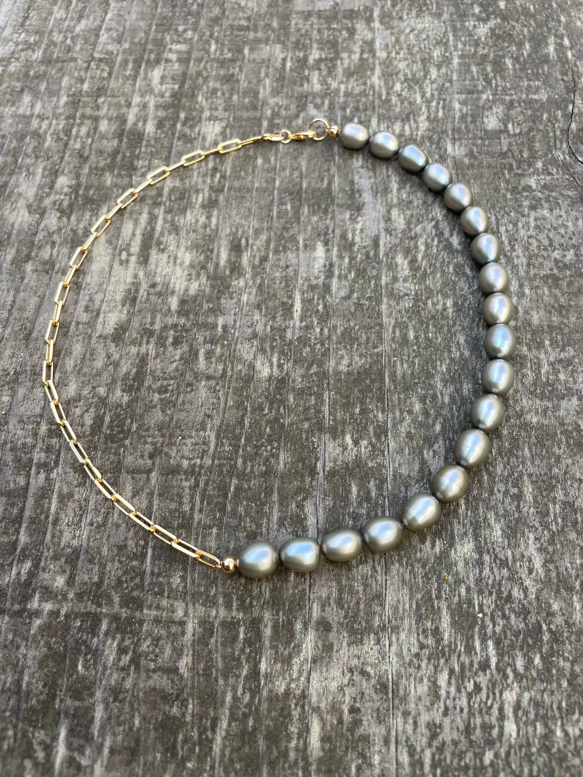 A choker necklace with half grey freshwater pearls and half gold chain on a wooden background