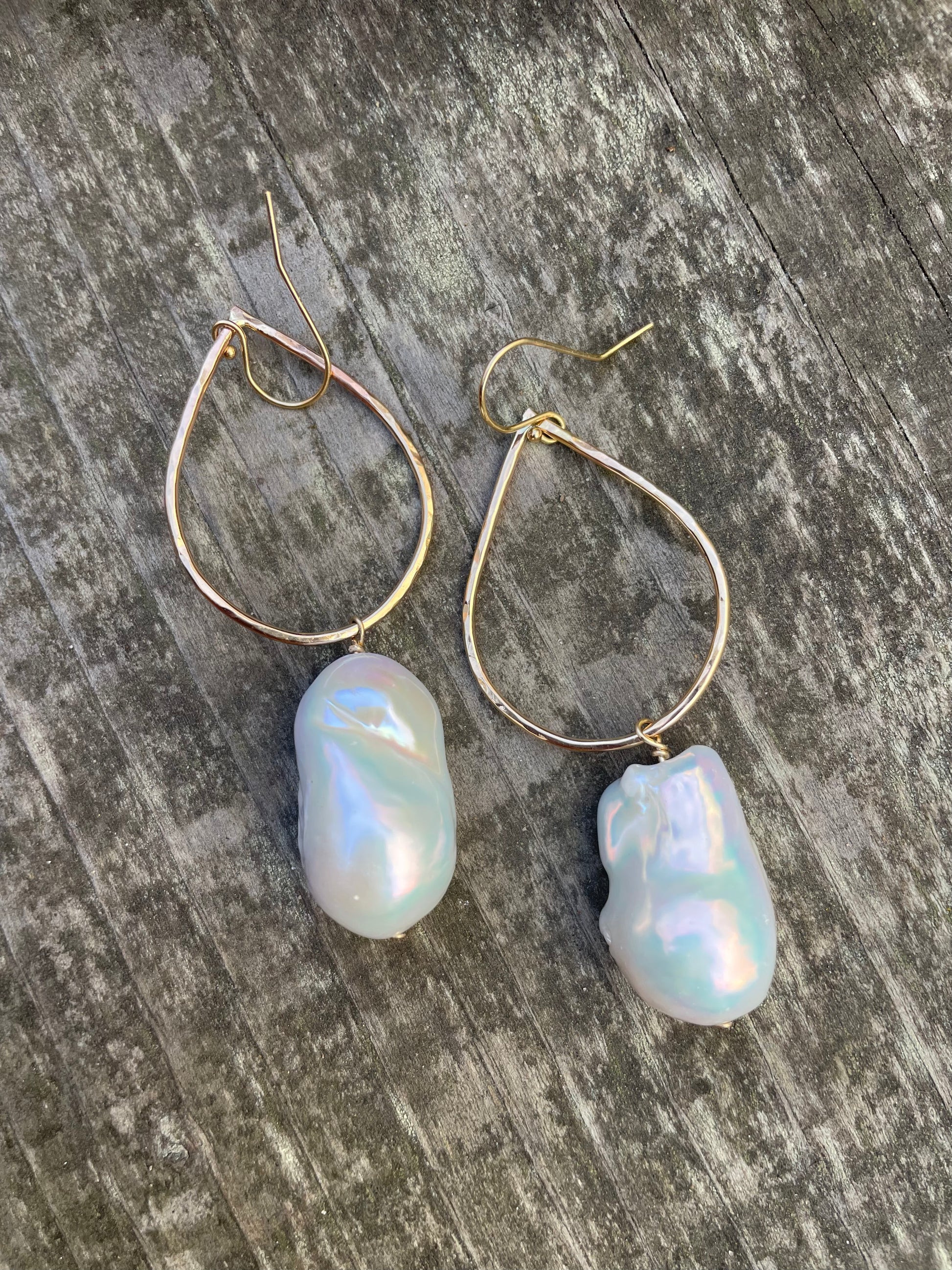 Large white baroque fireball pearls hanging off of a teardrop shaped gold wire with ear wires on a wooden background.