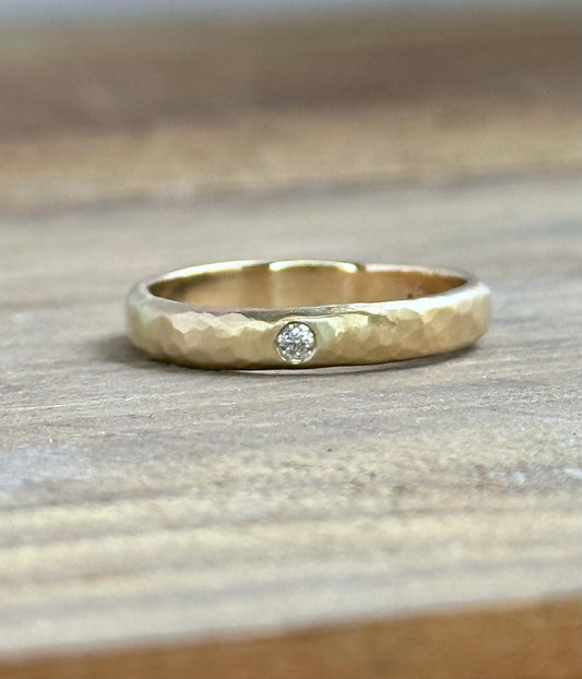 a gold textured ring iwth a single white diamond sits on a wooden background
