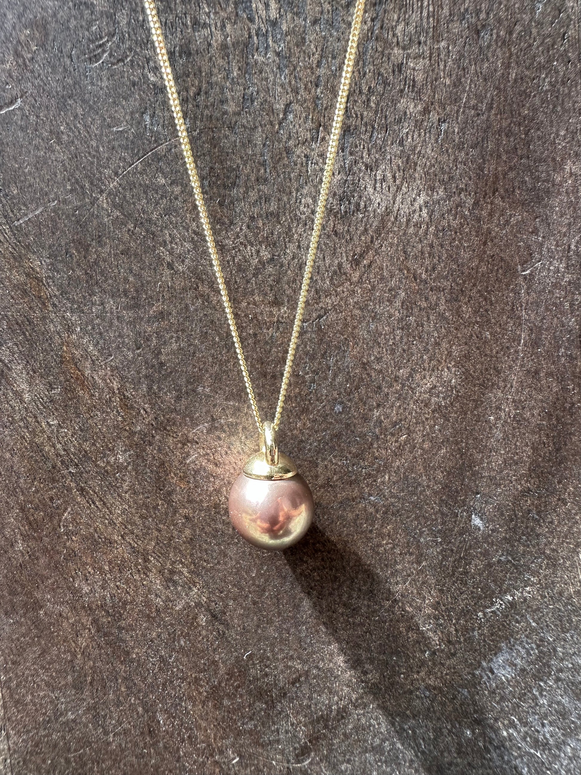 a copery pink round pearl necklace on a gold chain is on a grey wooden background