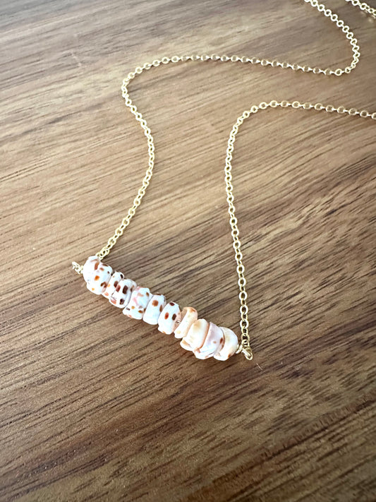 a bar of spottedpuka shells on a gold necklace on a wooden background