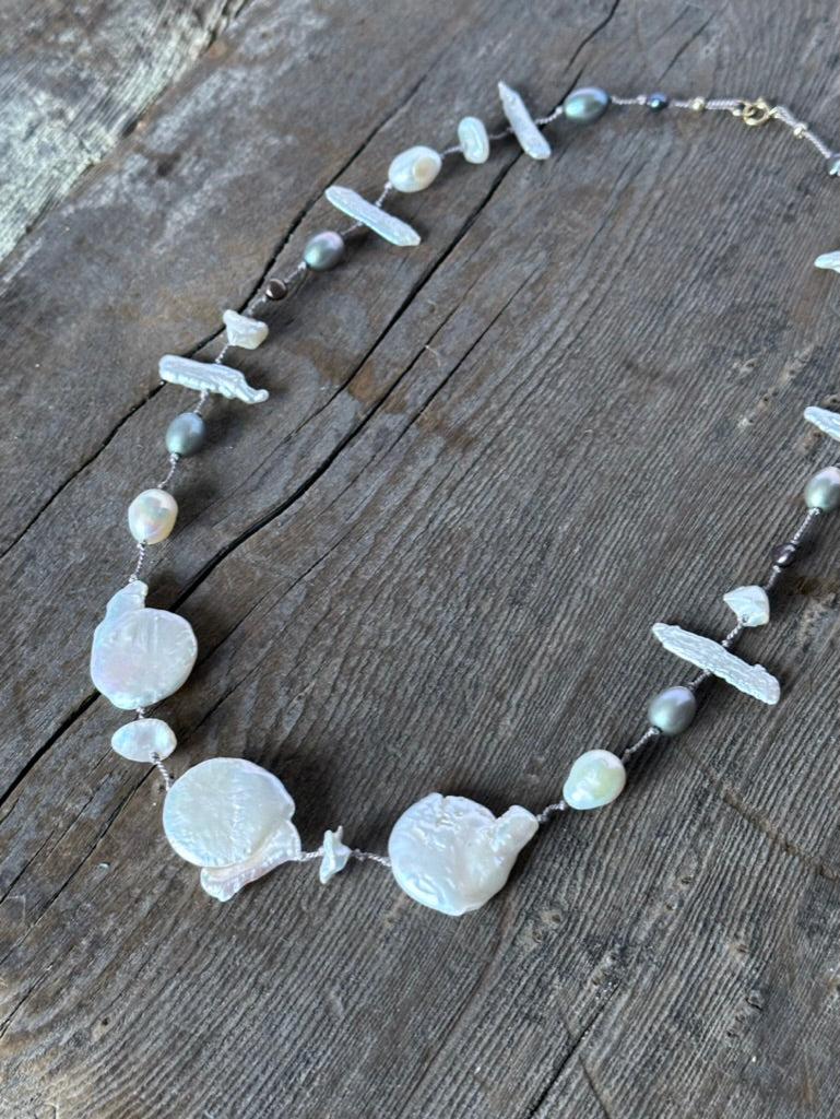 a necklace with three large cloud shaped white pearls and smaller white and grey perals on a wooden background.