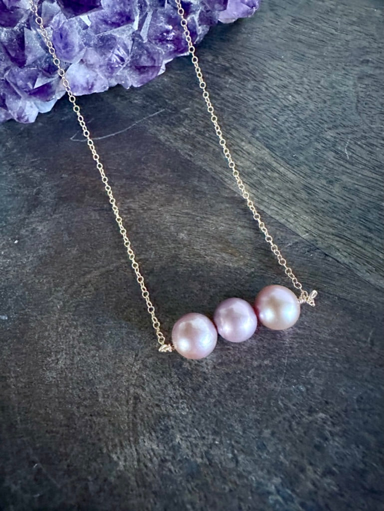 a necklace of three pink pearls on a wooden background on a gold chain with a purple amethyst in the upper left corner