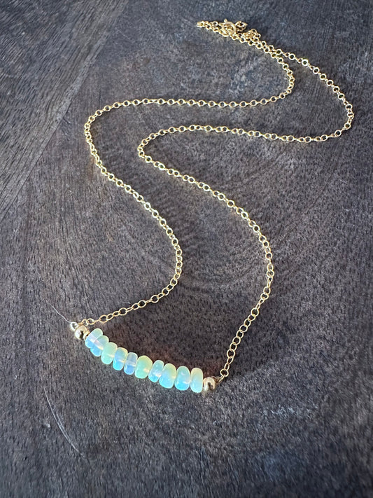 a necklace on wooden background. its on a gold chain with a bar of glowing bluish opals