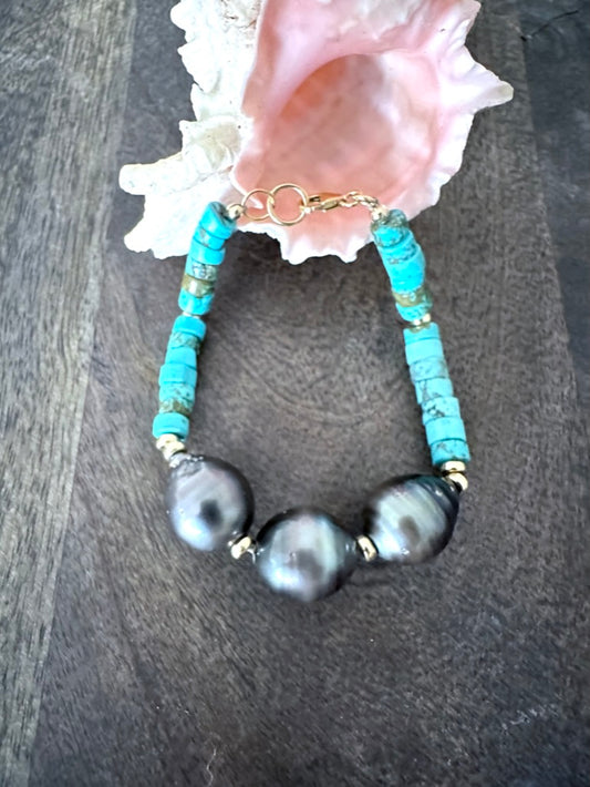 a turquoise and thre black pearl bracelet coming out of a pink shell on a woodenbackground.