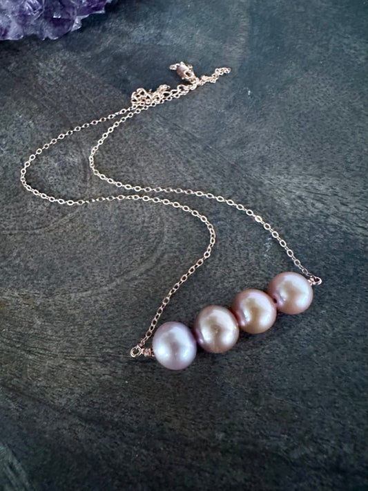a bar of pink pearls in graditing shades on a rosegld chain on a wooden background with a purple amethyst crystal in the upper left conrner